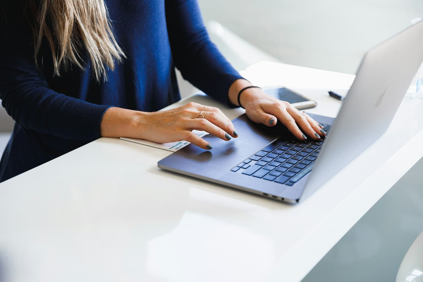 Hands typing on a laptop beside a phone and notes